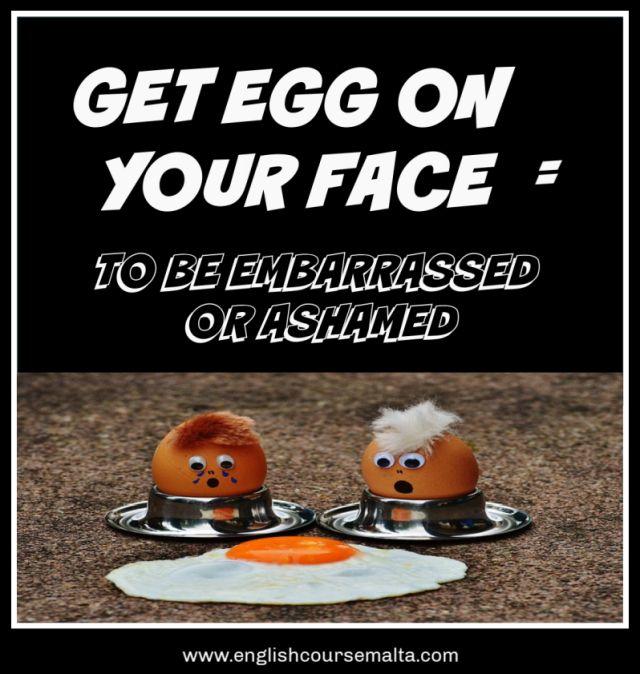 Picture with the words GET EGG ON YOUR FACE which is an idiom meaning to be embarrassed or ashamed. The photo shows two hard boiled eggs in egg cups with faces painted on on and a surprised expression. They are looking at a fried egg.